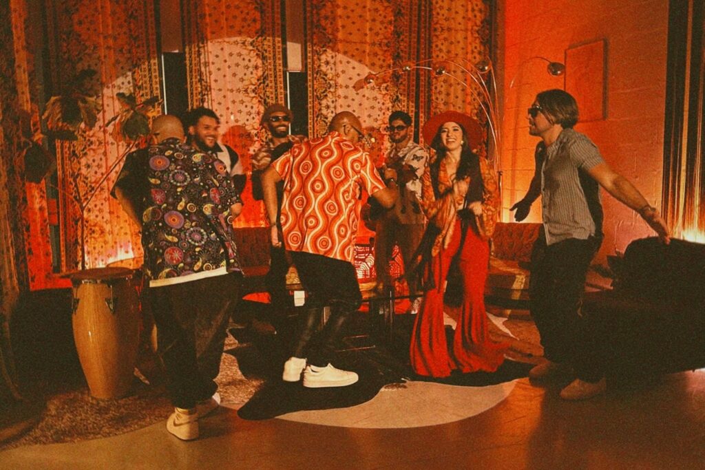 A group of friends dressed in 70s-era outfits dance in a dimly-lit space decorated in themes of the decade