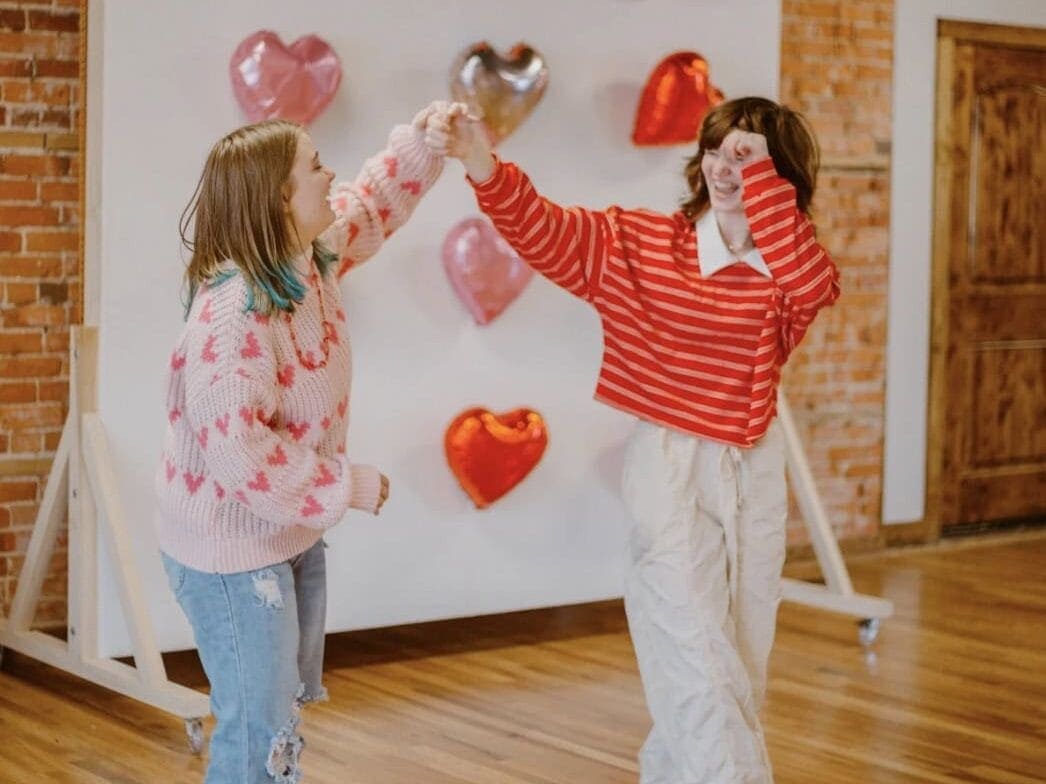 Two friends in sweater Galentines outfits in front of heart balloons