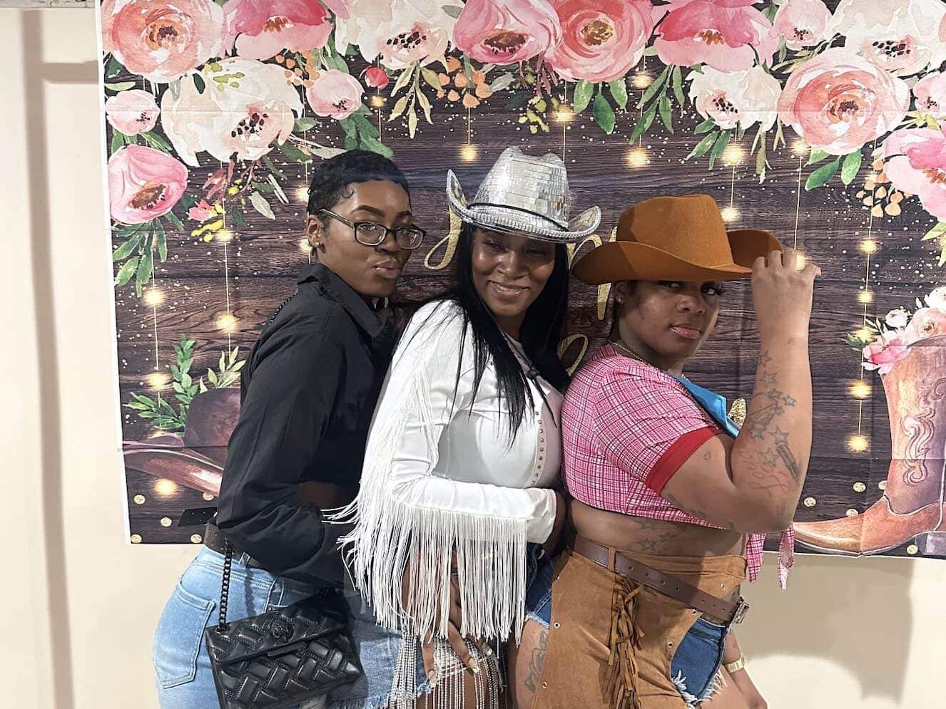 Three women dresses as cowgirls for cowboy theme party in front of a photo backdrop