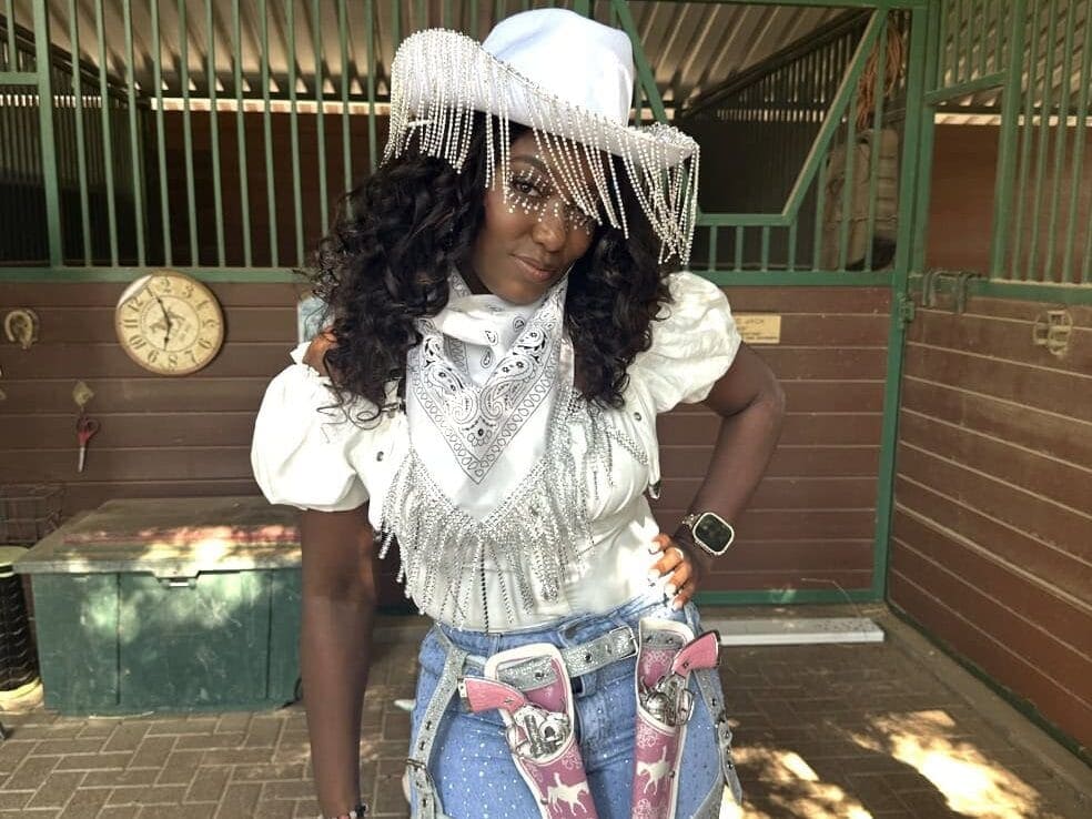 Woman in cowgirl party outfit with white cowgirl hat, fake pistols, denim
