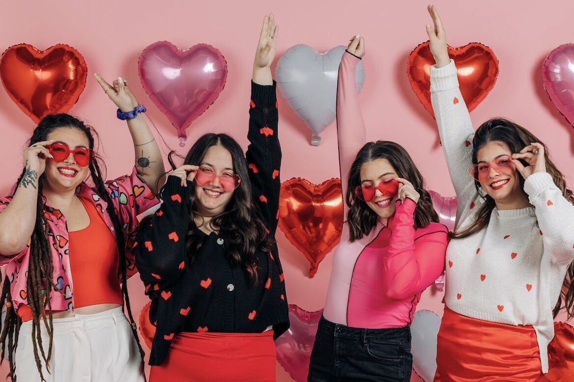 Four friends in heart themed outfits in front of balloon wall for Galentine's idea at home