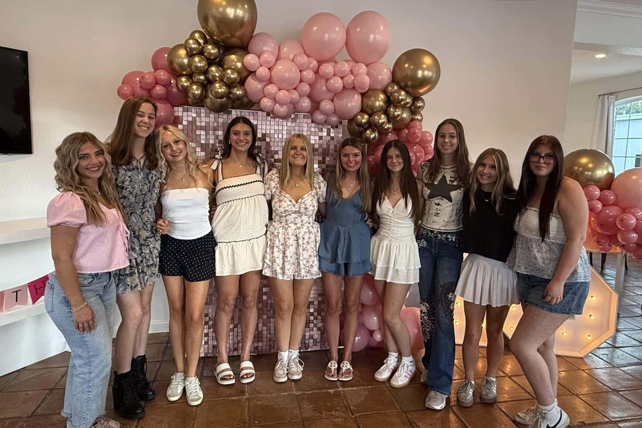Teen birthday party with friends posing in front of balloons and glitter wall backdrop