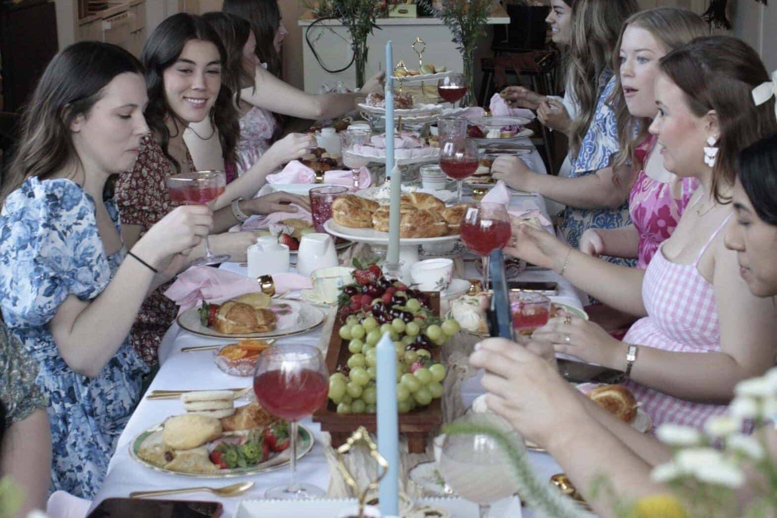 Group of friends around a table with food and decor for a tea party themed teen birthday