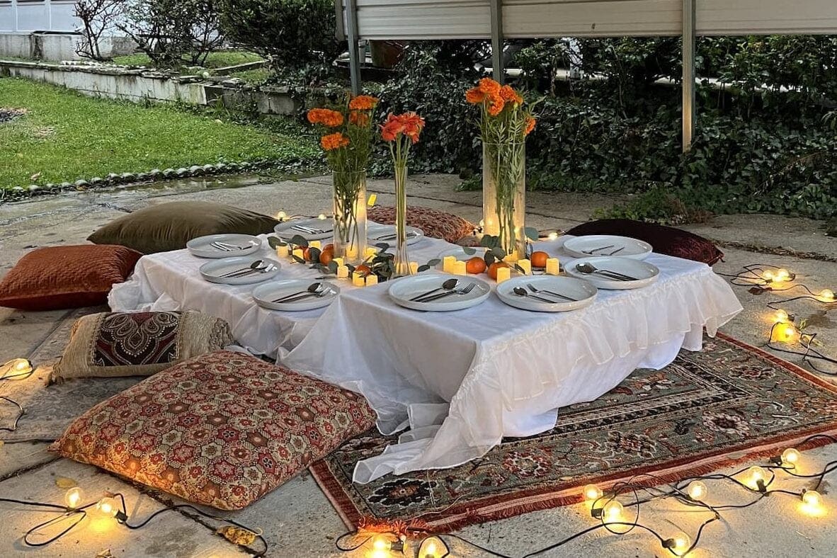 Pillows, lights, flowers, and low table set out for outdoor picnic as a mom's birthday idea