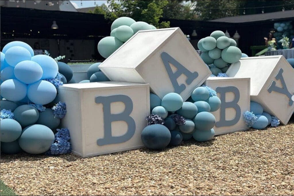 Blue balloons surround large blocks spelling out BABY at a boy-themed baby event