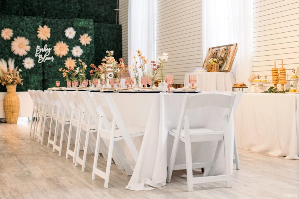Long guest table set up with pink glasses and sweet floral arrangements in front of a Baby in Bloom sign
