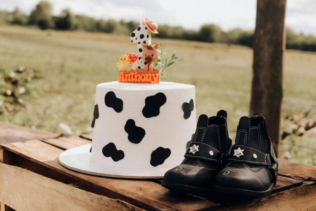 Tiny cowboy boots sit next to a cow-themed cake at a baby event