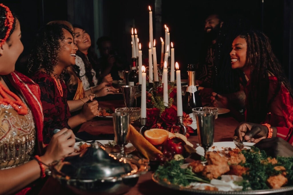 Friends share a festive meal at a table decorated in rich reds, oranges and greens with tall candles lit along the middle