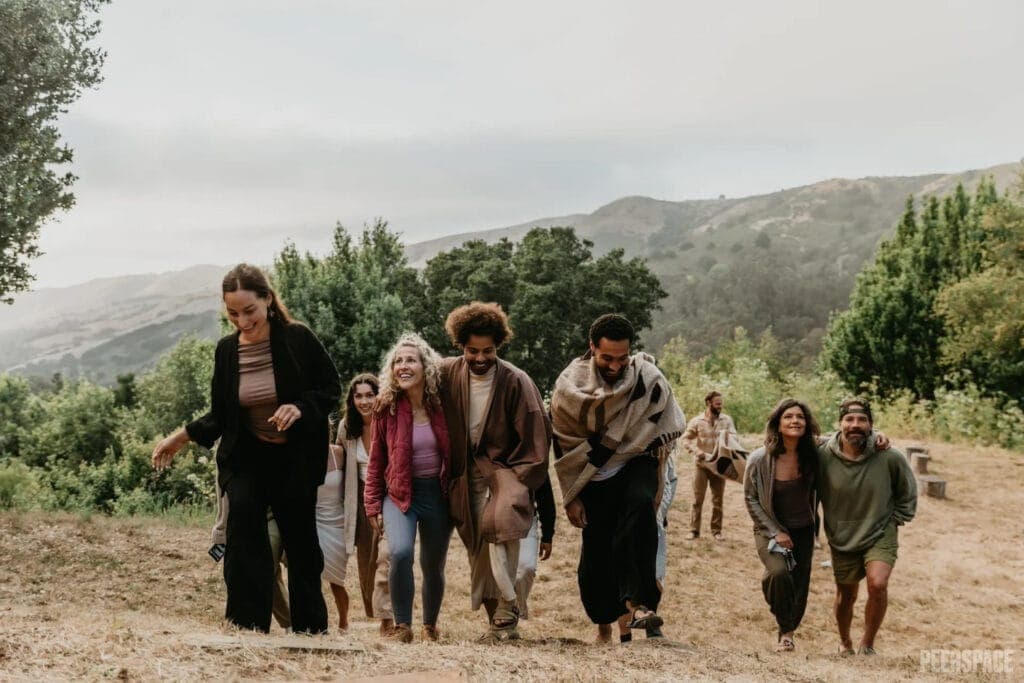 Friends in cozy sweaters and wrapped in blankets walk up a hill together