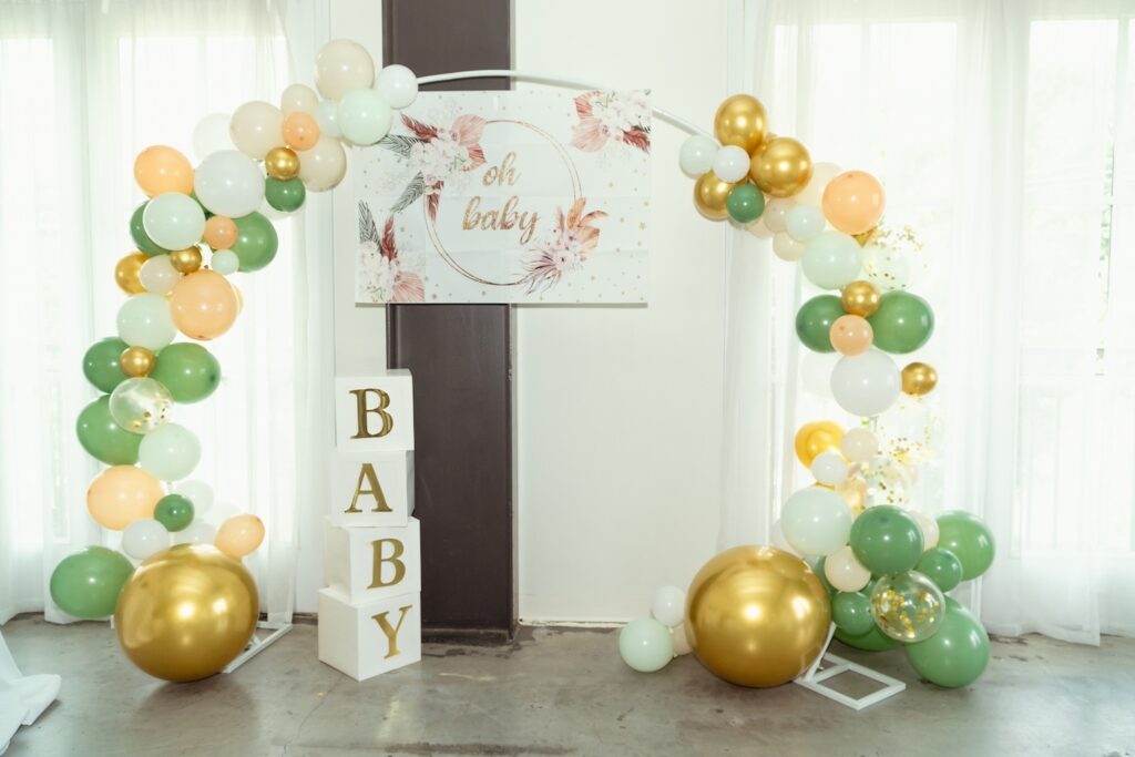Green, gold and neutral balloons decorate an archway at a baby event
