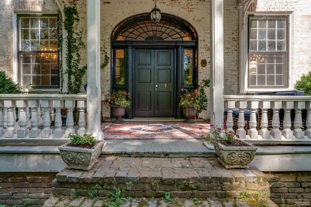 Grand entrance of a historic home is flanked by potted flowers and ivy