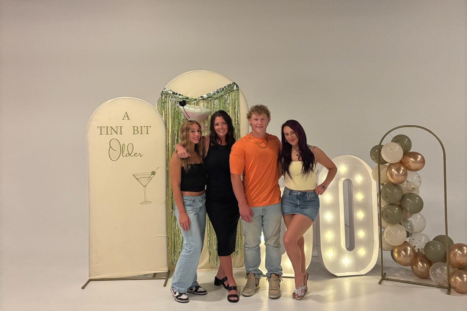Family posing in front of birthday decor including signs and balloons for mom's birthday party