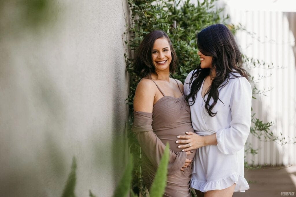 A mom-to-be stands with a friend and smiles at the camera