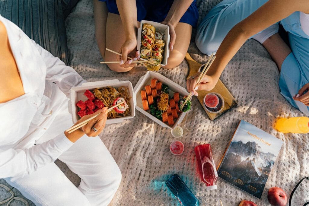 Photo from above of three people eating sushi at a birthday party picnic