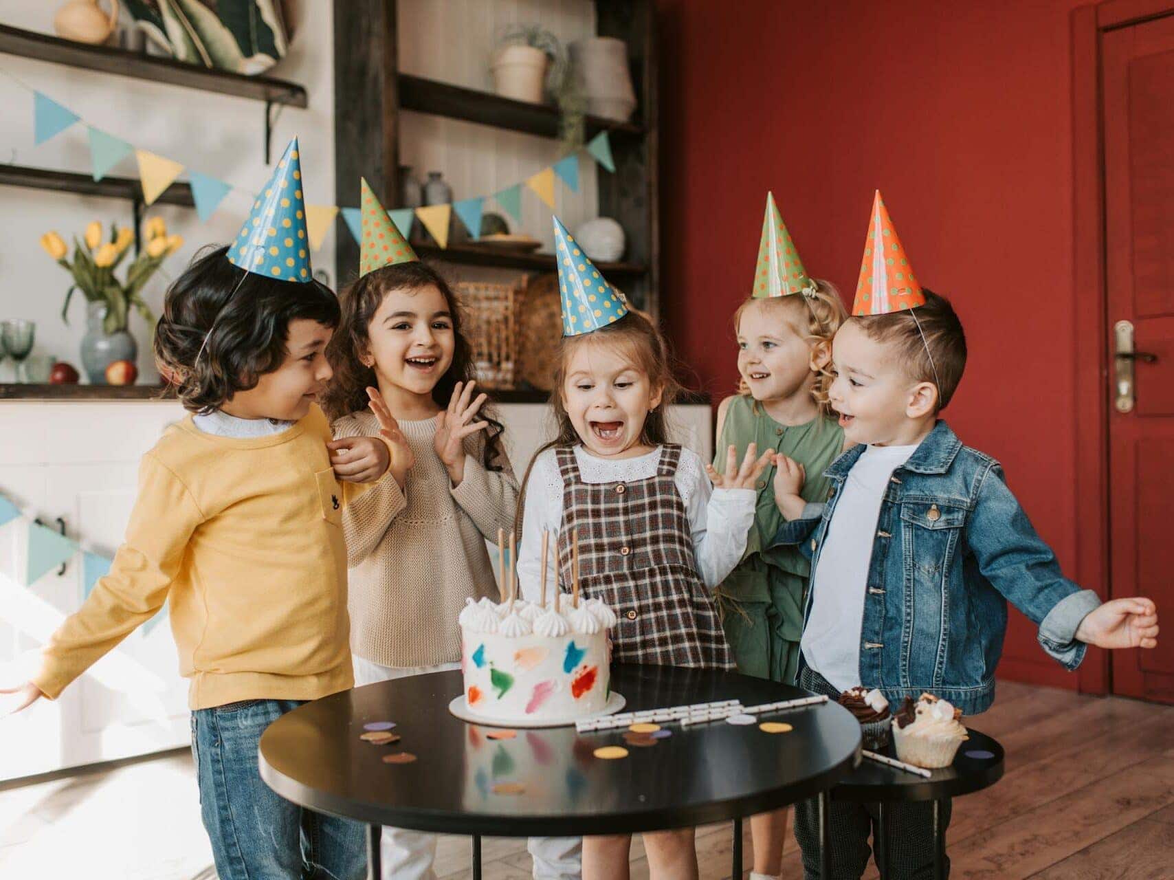 Group of children at indoor birthday party with party hats and birthday cake