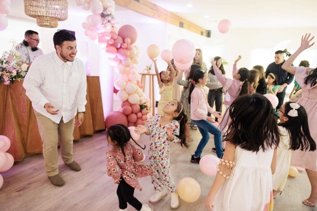 A bunch of kids on a dance floor reaching for pink and yellow balloons